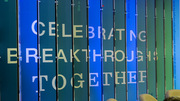 The wall features the words “Celebrating Breakthroughs Together” from one angle and photos and bios of honorees from the other side.
