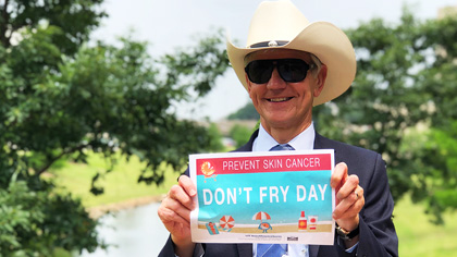 Man in cowboy hat and sunglasses holding up a sign that says Don't Fry Day