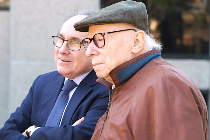 Two gray-haired men wearing glasses. One man is wearing a golf hat.