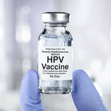 Someone holding a bottle of HPV vaccine with two gloved fingers