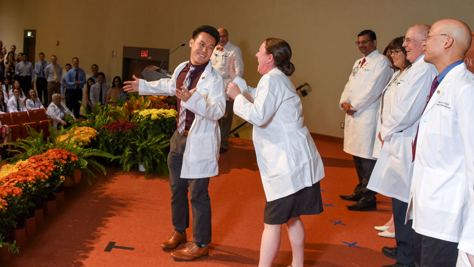 A student and faculty laugh during the White Coat Ceremony