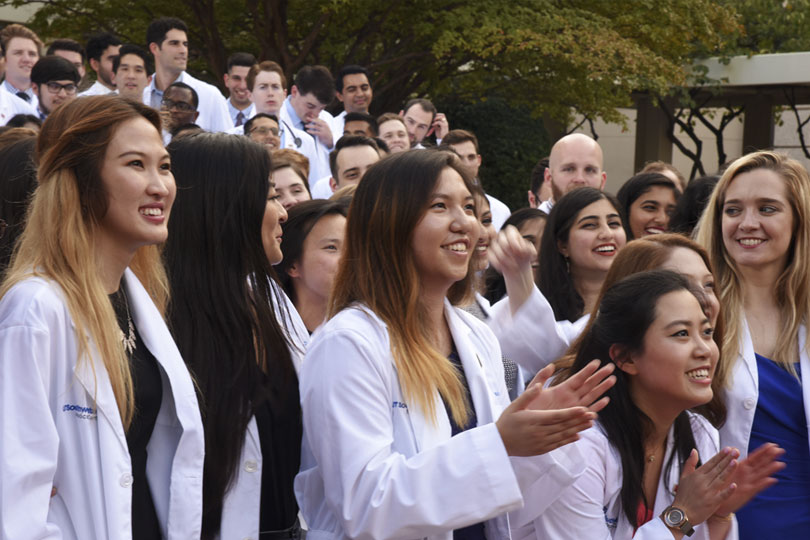 Students in white coats stand in a group outside