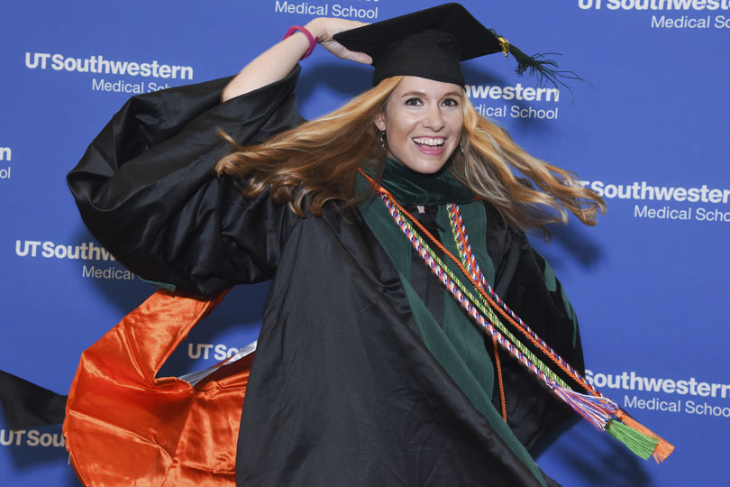 A student wearing her cap and gown spins quickly to the side