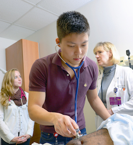 First-year medical student Michael Zhou practices an abdominal exam as Dr. Elizabeth Brickner explains the procedure to other Cary College members.