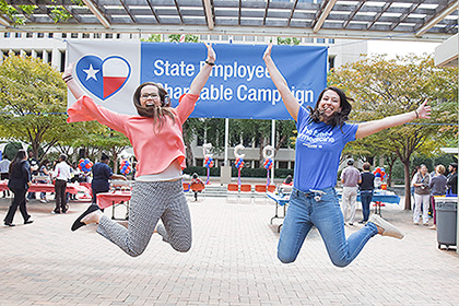 A woman and a man jump in the air in front of the SECC banner on the South Campus