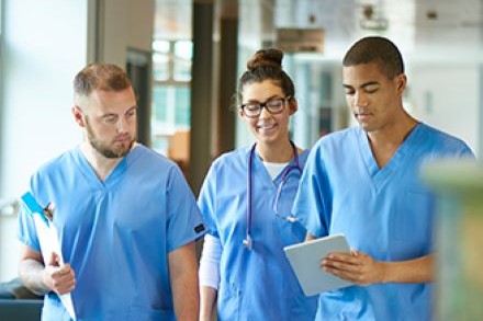 3 young medical students in blue scrubs walk together