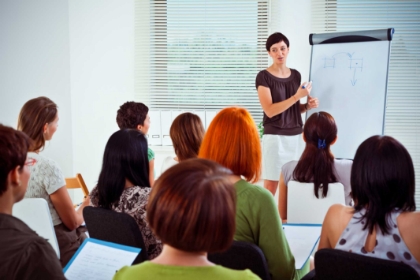 Students seated in classroom facing instructor who is pointing to a whiteboard
