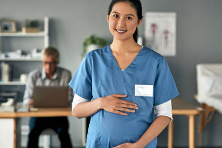 Photo of male with his arm around a female, sitting on a couch and smiling while looking at the female's baby bump.