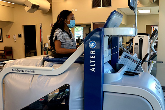 Young black woman working on a large blue machine wearing a face mask.