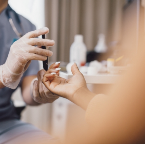 medical professional wearing gloves does a blood test on female patient's finger