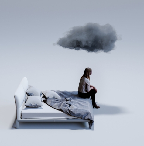 woman sits at on a bed, dark cloud over her head
