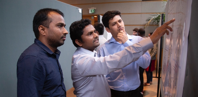 A man points to a board as he talks with two male students 