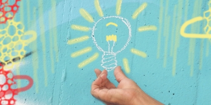 A hand under a chalk drawing of a light bulb