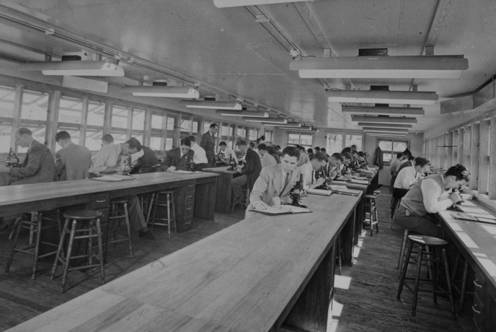 Southwestern Medical College students bent over microscopes with empty tables in foreground (circa 1944).