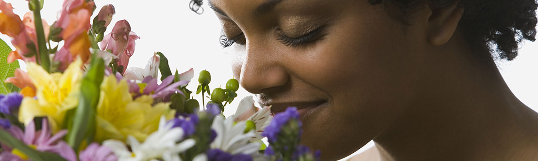 young woman smiles and closes eyes as she smells a bouquet of colorful flowers