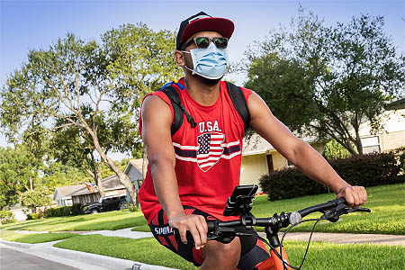 A man riding his bike with a mask, sunglasses, and hat