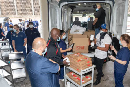 Men and women in masks unload packaged food donations from a truck