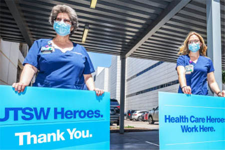 Female nurses in blue scrubs hold signs thanking health care heroes