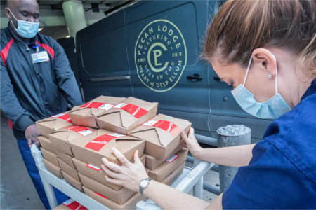 A man and a woman push a cart filled with boxes of donated food