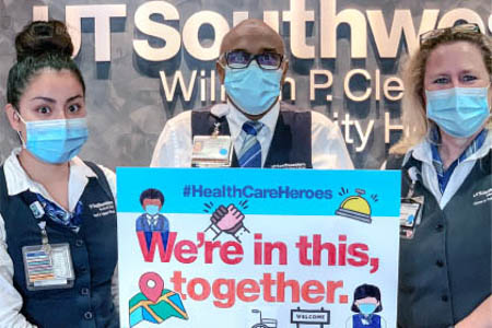 A man and two women hold a sign that says We're In This, Together