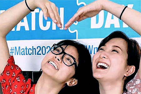 Two women smiling, making a heart shape with their arms