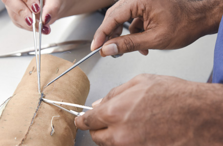 A man and a woman practice suturing on a model arm