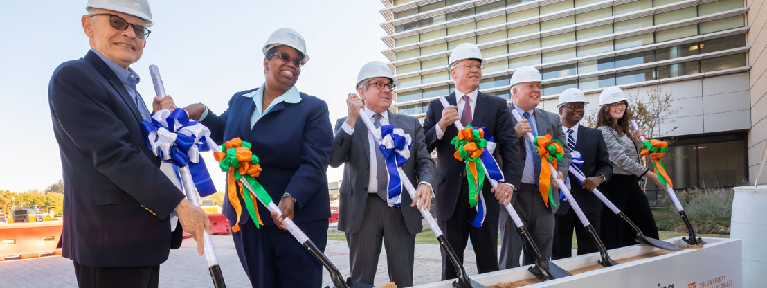 Seven men and woman wear hard hats and hold shovels as they break ground for a new Biomedical Engineering building