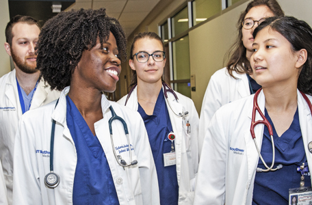 A diverse mix of men and woman in blue scrubs and white coats