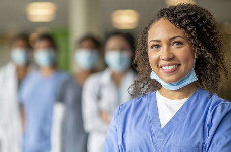 A woman with brown hair wearing blue scrubs and her mask under her chin