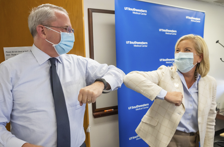 A male and a female hospital executive wear masks and bump elbows