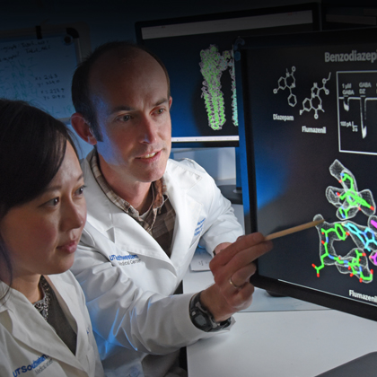 A male and a female researcher examine pink, blue, and green lines on a computer monitor