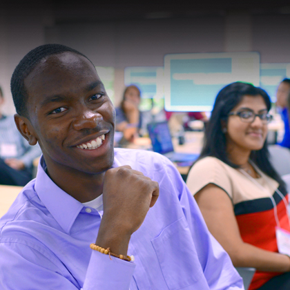 A man wearing a purple dress shirt smiling in a classroom