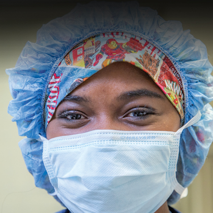 A woman in blue scrubs, a cap, and a face mask