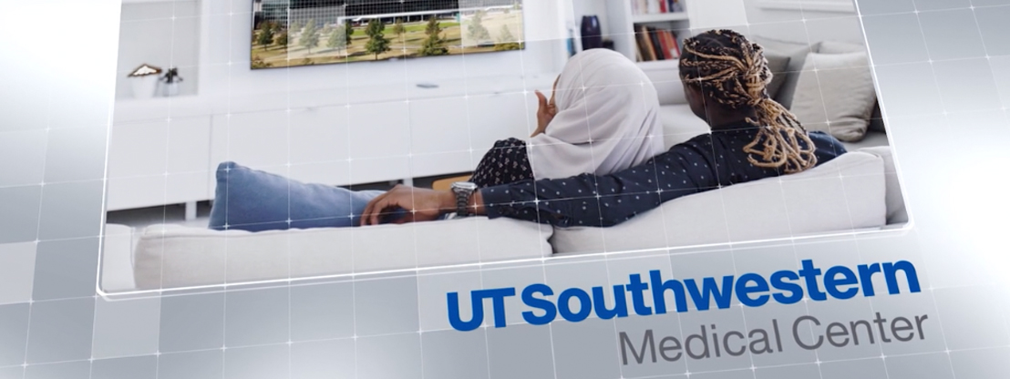 UT Southwestern Medical Center: Back view of a man with long braids sitting on a couch with his arm around a woman wearing a head scarf watching TV
