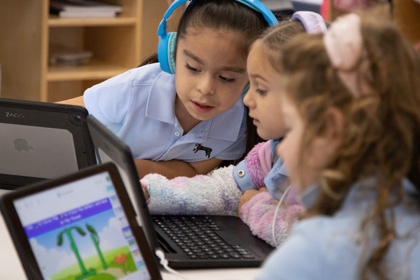 Three female children wearing headphones looking at laptop screen