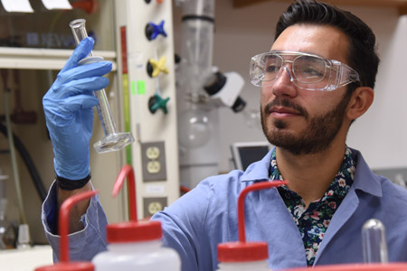 A man wearing protective eyewear, while holding a test tube and examining the results