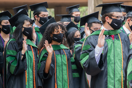 A group of students wearing green and black cap and gowns while wearing face masks