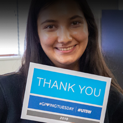 A female with brown hair, holding a Thank You sign on Giving Tuesday