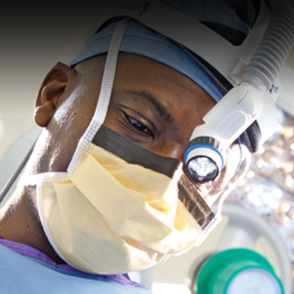 A man in blue scrubs, a cap, and a face mask