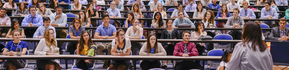 A professor with a white shirt speaking with students in a classroom