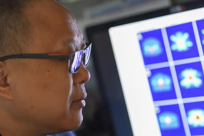 close up of man with glasses looking at images on computer screen