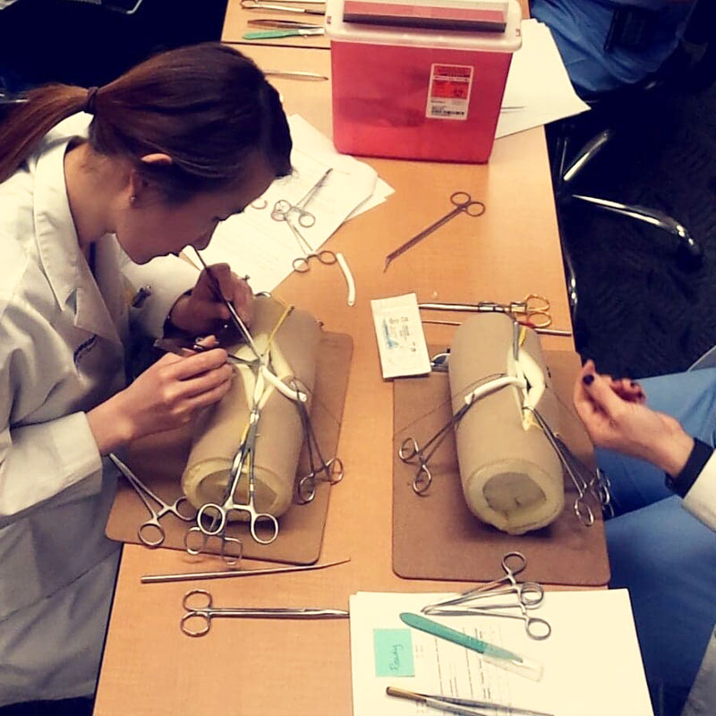 Two general surgery residents practice vascular surgery on a large foam roll