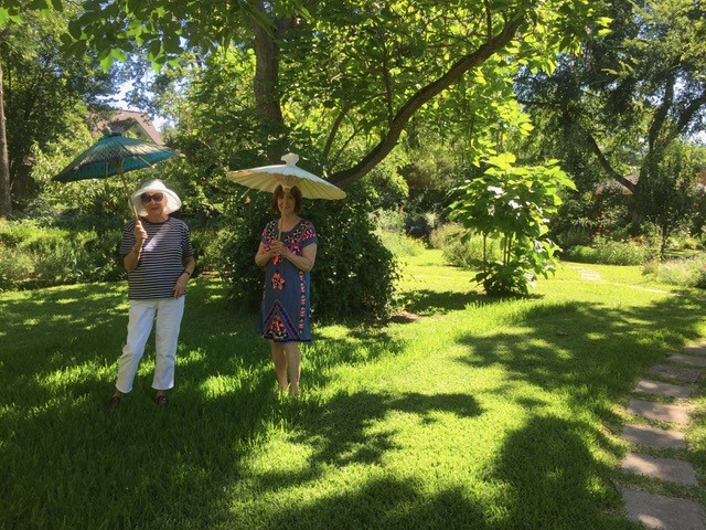 two women walking in a lush garden with parasols