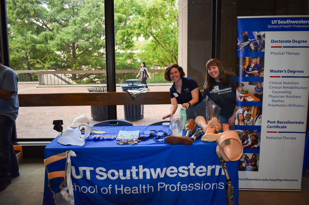 Two female students stand behind a table where prosthetic legs and feet lie.