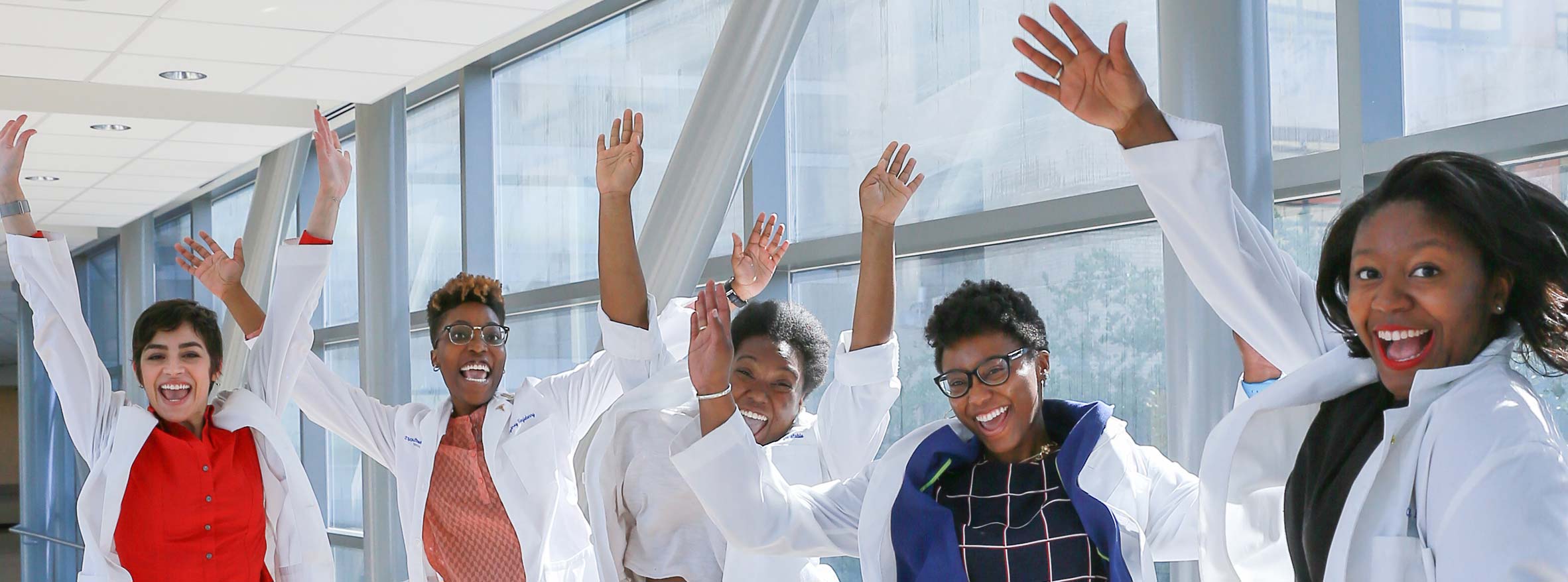 Five female students in white coats wave