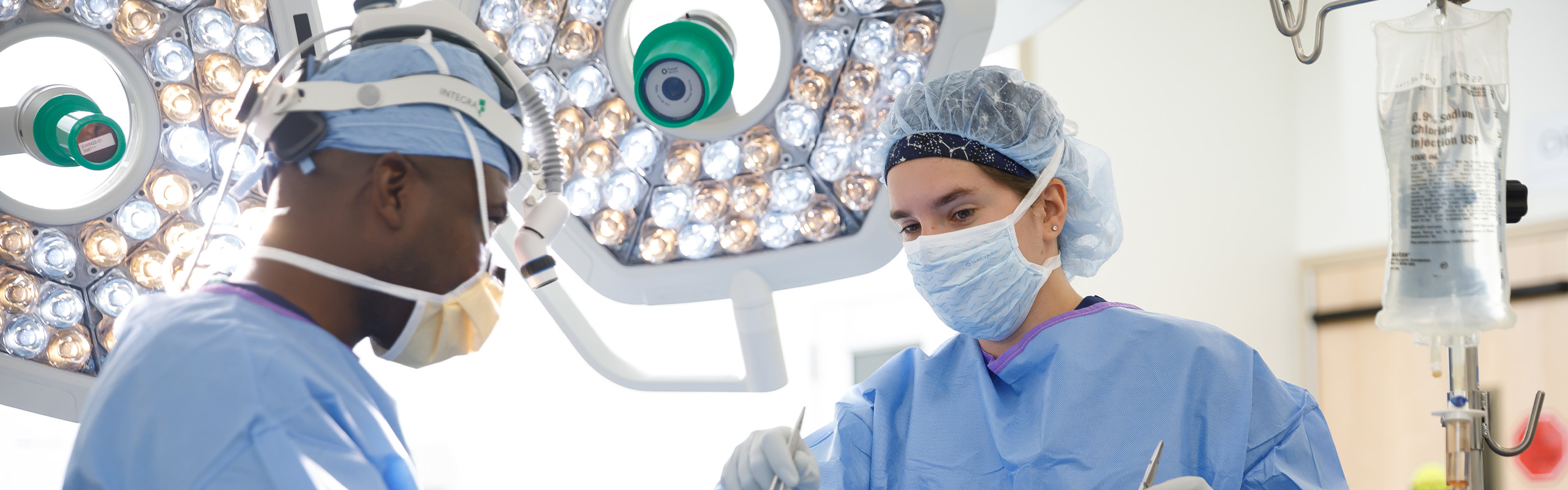 Two doctors in operating theater, wearing surgical gear, working on covered patient.