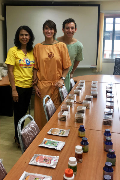 aylore King and two colleagues stand by tables of packets and bottles of traditional Thai remedies and healing techniques
