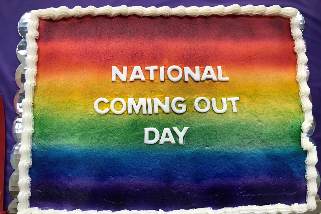 A rainbow striped cake with National Coming Out Day written on it