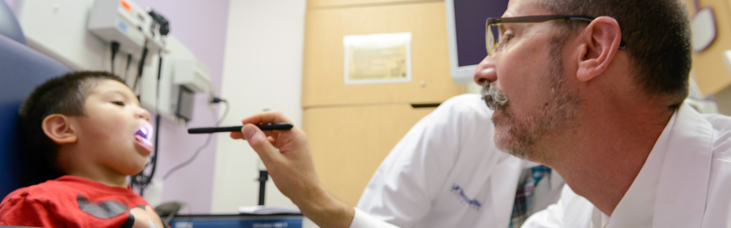 Dr. using a penlight to examin a small child's mouth.