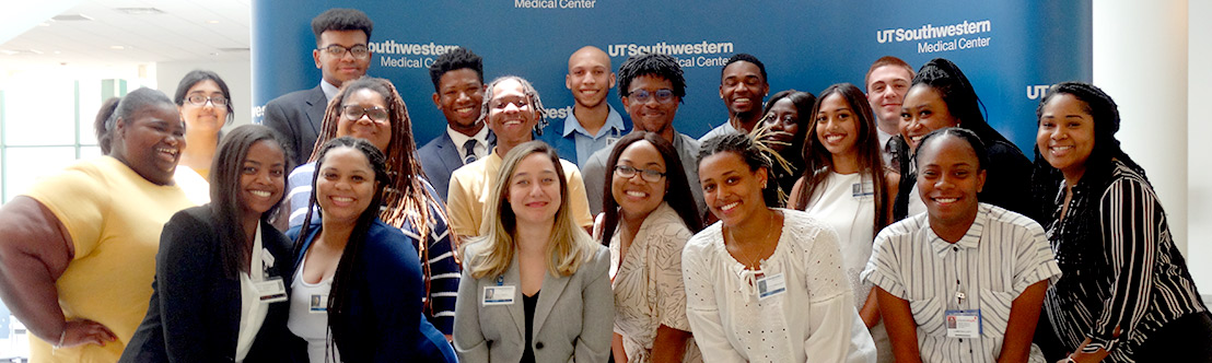 Diverse group of smiling young people wearing badges in front of a UT Southwestern Medical Center wall